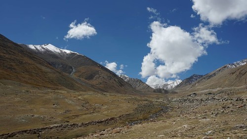 Extensive valley with meadows under a clear blue sky and white clouds, trekking in Ladakh,