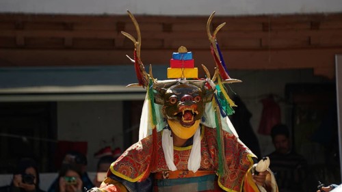 A dancer wears a decorative animal mask with antlers and colorful clothing during a traditional