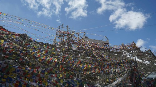 A network of colorful prayer flags stretched at Khardung-La Pass under a blue sky, trekking in