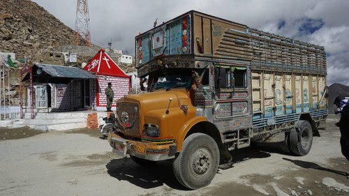 Colourful truck at Khardung-La Pass next to other vehicles and small houses with Indian flag under