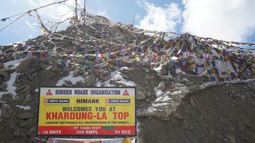 Colourful prayer flags fly next to the Khardung-La Top sign on the summit, trekking in Ladakh,