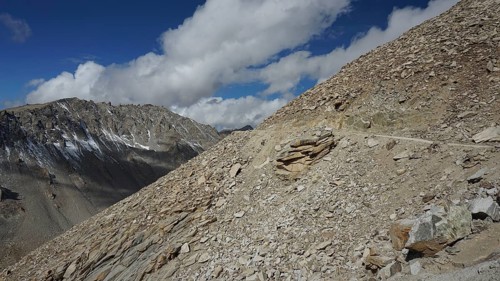 Rocky mountain terrain with road on the mountainside under a sunny sky with scattered clouds,