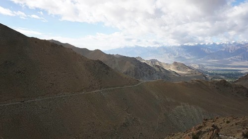 A road along a rocky mountainside that runs through a vast landscape under clear skies, trekking in