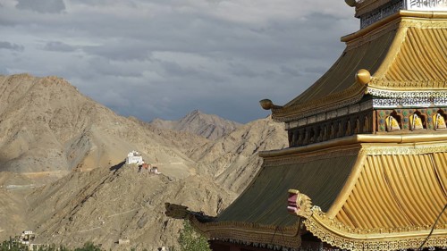Roof of a Tibetan Buddhist temple with mountain backdrop and dramatic sky, trekking in Ladakh,
