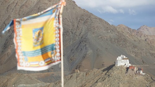 Tibetan Buddhist prayer flag with Namgyal Tsemo Buddhist monastery surrounded by mountains and sky,