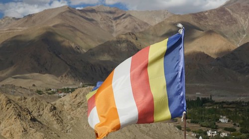Colorful international Buddhist flag in a mountainous landscape over a green valley, Leh, trekking