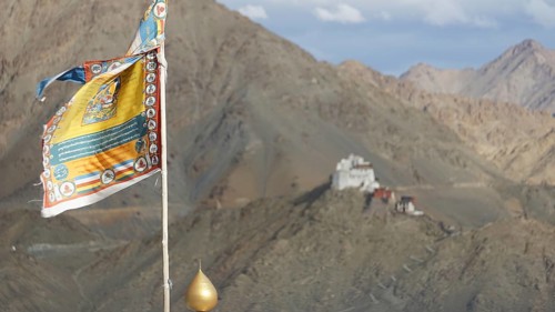 Colourful Buddhist flag with Namgyal Tsemo Buddhist monastery surrounded by mountains and sky, Leh,