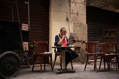 Cairo, Egypt. June 14th 2024 An Egyptian man smokes, drinks tea and reads a newspaper in local café