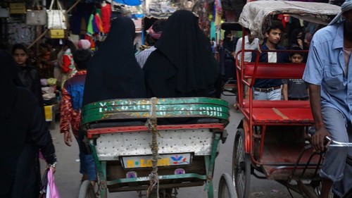 A hustle and bustle of rickshaws and people passing by on a narrow street in the Muslim quarter of