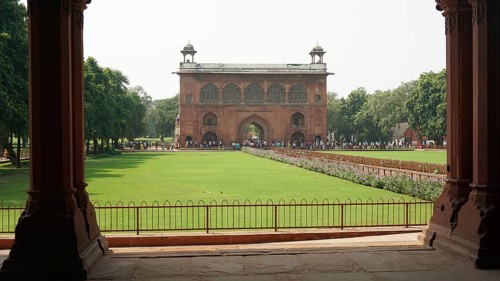 Historic gate with green lawn and trees, Red Fort in Delhi with numerous visitors in the area,
