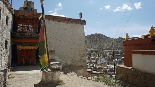 Houses and a colorful big prayer flag with mountains in the background under blue sky, Leh, city