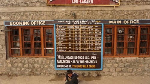 Stone building at the bus terminal with a large timetable on the façade and signs for Leh, Ladakh,