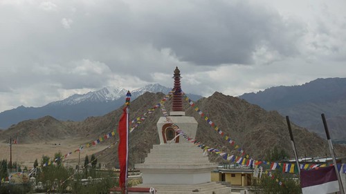 A stupa in Leh, surrounded by colorful prayer flags and mountain panorama in the background, Leh,