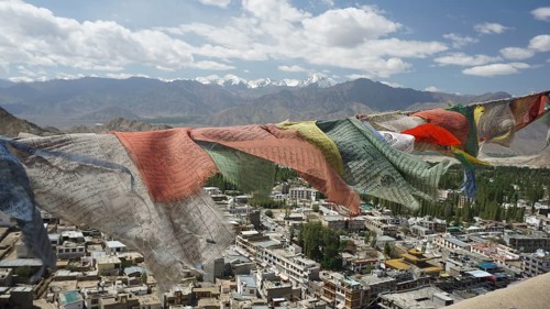 Prayer flags fly over Leh, a city with mountains and cloudy sky in the background, view from Leh