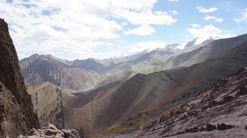 Panoramic view of a mountainous landscape with rolling hills and snow-capped peaks on the horizon,