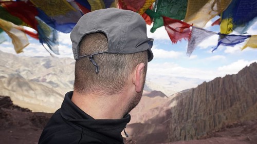 Person looking at a vast mountain landscape under fluttering prayer flags, trekking at Stok La Pass