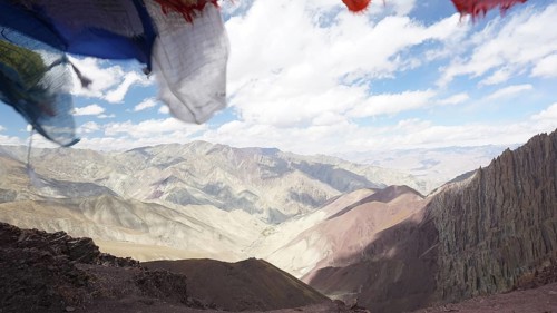 Prayer flags in front of a vast, cloud-covered mountain landscape, trekking at Stok La Pass in
