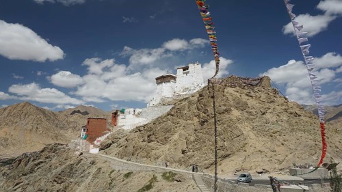 A mountain monastery perches on a rocky hill under a clear sky with floating prayer flags, Ladakh,