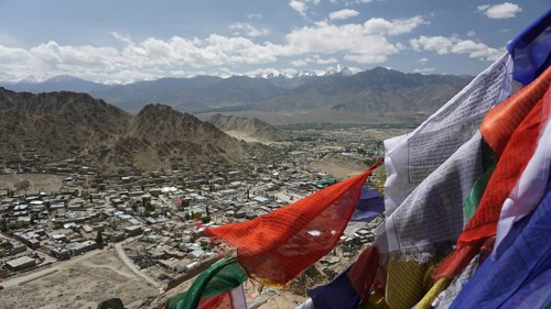 City view with prayer flags in the foreground and mountain scenery in the background under blue
