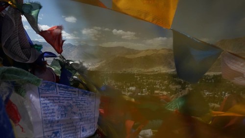 Colourful prayer flags fly against a vast mountain landscape and blue sky with clouds, Ladakh,