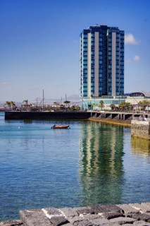 Modern high-rise building reflected in calm water, urban ambiance under clear skies, Arrecife,