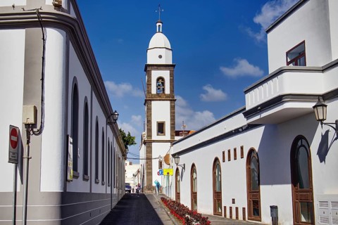 White buildings with church tower of the Iglesia de San Ginés church along a paved street under