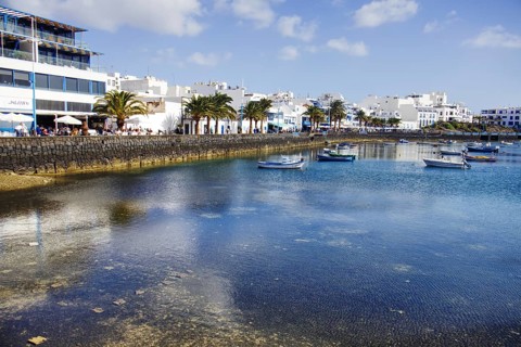 Boats on the calm waters of the Charco de San Ginés lagoon surrounded by palm trees and white