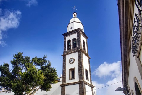 White church tower with clock of the Iglesia de San Ginés church under blue sky, surrounded by