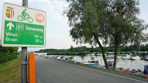 Signpost on Danube trail R1 with river and boats in the background, cycling on the Danube cycle