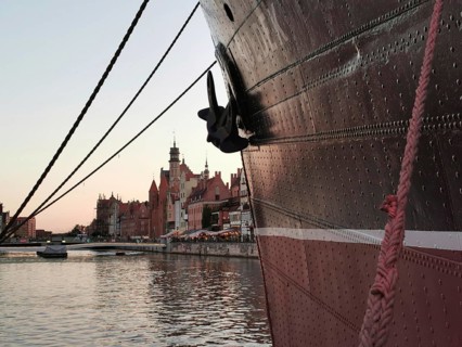 Looking along the bow, a large ship is moored in the harbor in front of the picturesque, historic