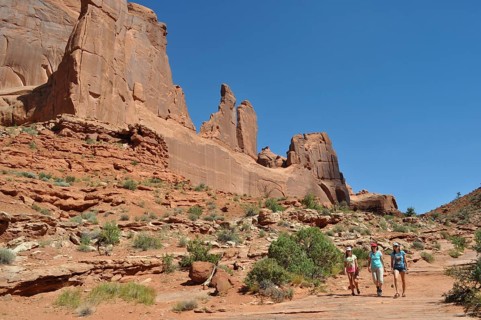 Several people are hiking in a dry, rocky landscape called Wall Street, under a bright blue sky,