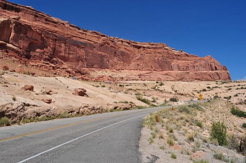 Road leading past a barren, red rock formation under bright blue sky, Arches National Park, Utah,