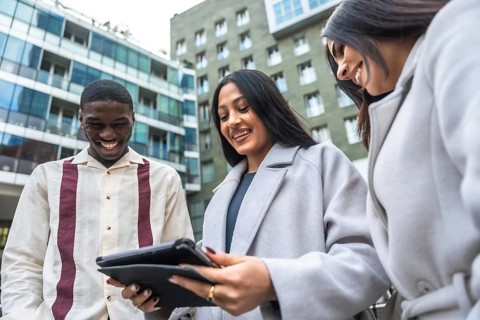 Diverse business colleagues smiling and laughing while collaborating over a tablet outdoors by