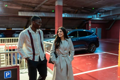 Smiling multiracial couple walking through a modern parking garage with bright red floor and cars,