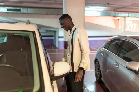 Young black man in an underground parking garage smiling as he opens his white car door, confident