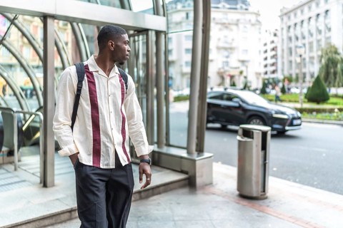 Young black man carrying a backpack and wearing a stylish shirt, standing confidently on a city