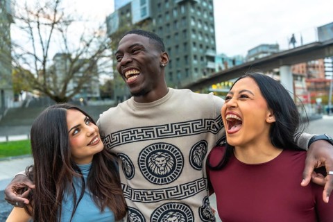 Three multiethnic friends laughing and embracing on a city street, sharing joyful, candid moments
