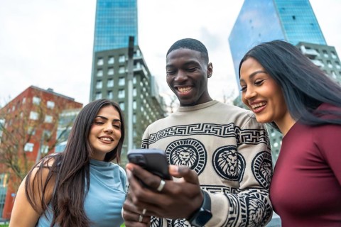 Group of diverse young adults laughing while looking at a mobile phone screen together, sharing a