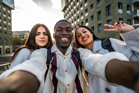 Three smiling multiracial friends enjoying an outdoor moment, capturing a joyful selfie together in