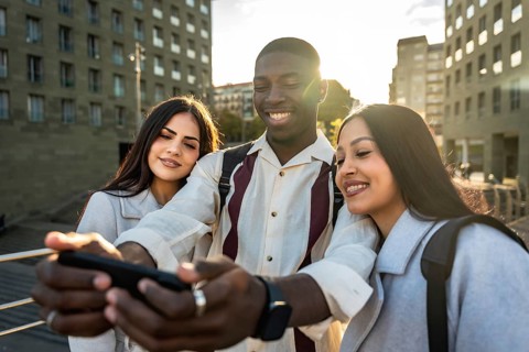 Diverse group of young friends is smiling and laughing together while taking a selfie with a