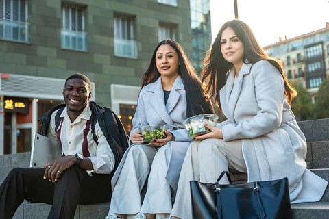 Diverse colleagues sitting on steps and smiling while enjoying healthy salads during a casual urban