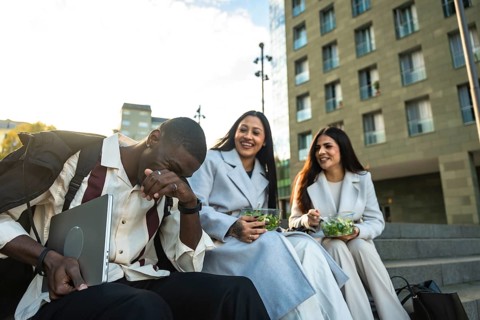 Diverse colleagues enjoying their lunch break outdoors, sitting on stairs in the city, laughing and