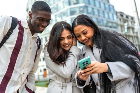 Diverse group of young adult friends smiling and laughing while watching something on a smartphone