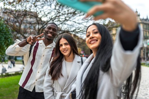 Happy diverse friends smiling and posing for a cheerful selfie with a smartphone outdoors in a city