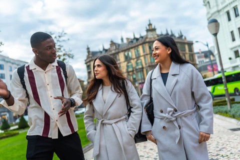 Three diverse young adult friends walking together outdoors in an urban city park, having an