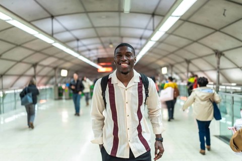 Young african man smiling, wearing a backpack and casual clothes, walking confidently through a