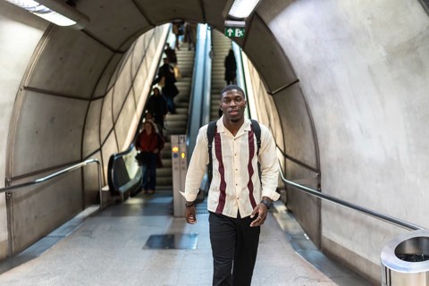 Young man with backpack walking confidently through a modern subway tunnel past escalators and