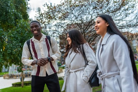 Multiracial young adults walking together in an urban park, smiling and happily conversing, showing