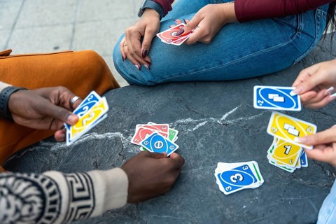 Diverse people gathering outdoors, playing a popular card game, throwing cards onto the stone