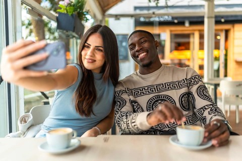 Happy diverse couple smiling while taking a selfie with a smartphone at a coffee shop, enjoying